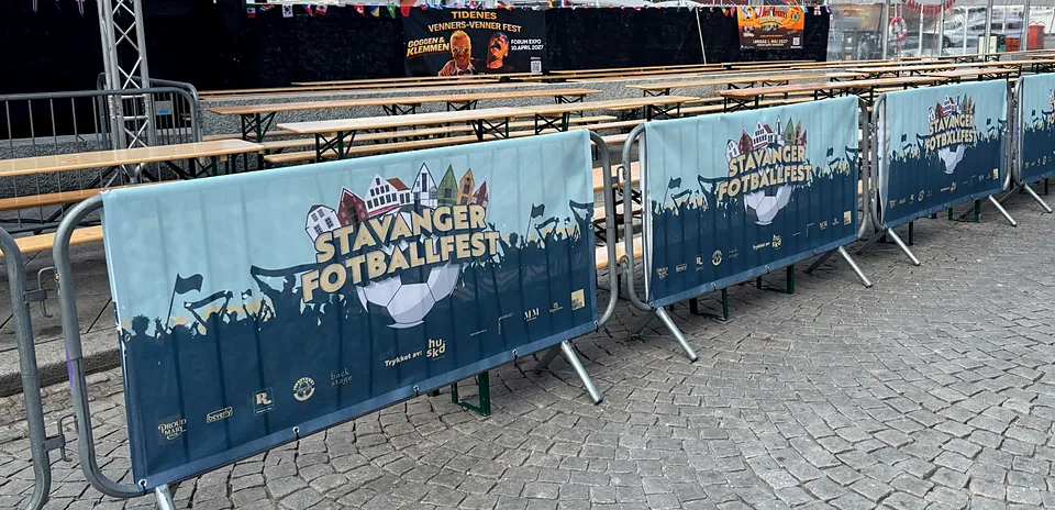 Fire like bannere med Stavanger Fotballfest-logo festet på sperregjerder foran langbord på Torget i Stavanger.