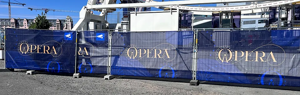 Mørkeblå gjerdebannere med Opera-logo montert på byggegjerde ved pariserhjulet i Bispevika i Oslo.