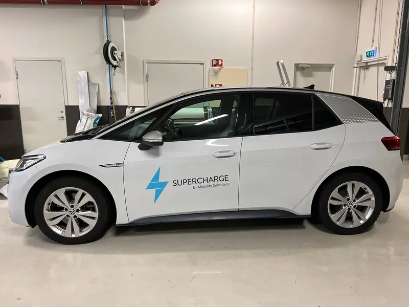 Hvit elbil med logo og navnetrekk på fordøren